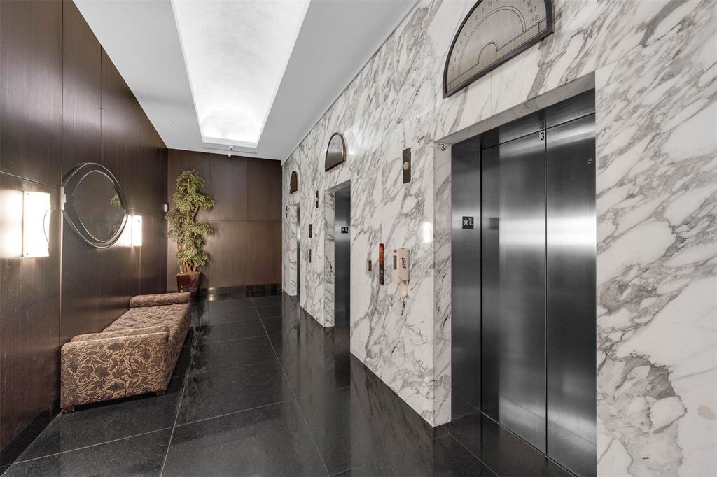 A modern elevator lobby features marble walls, dark flooring, a patterned bench, and recessed lighting — 100 S EOLA DRIVE UNIT 1005, ORLANDO, FL