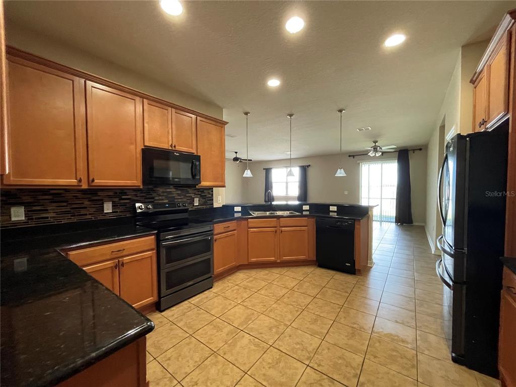 A kitchen features wood cabinets, black appliances, dark countertops, and tile flooring — 10026 WEATHERS LOOP, CLERMONT, FL