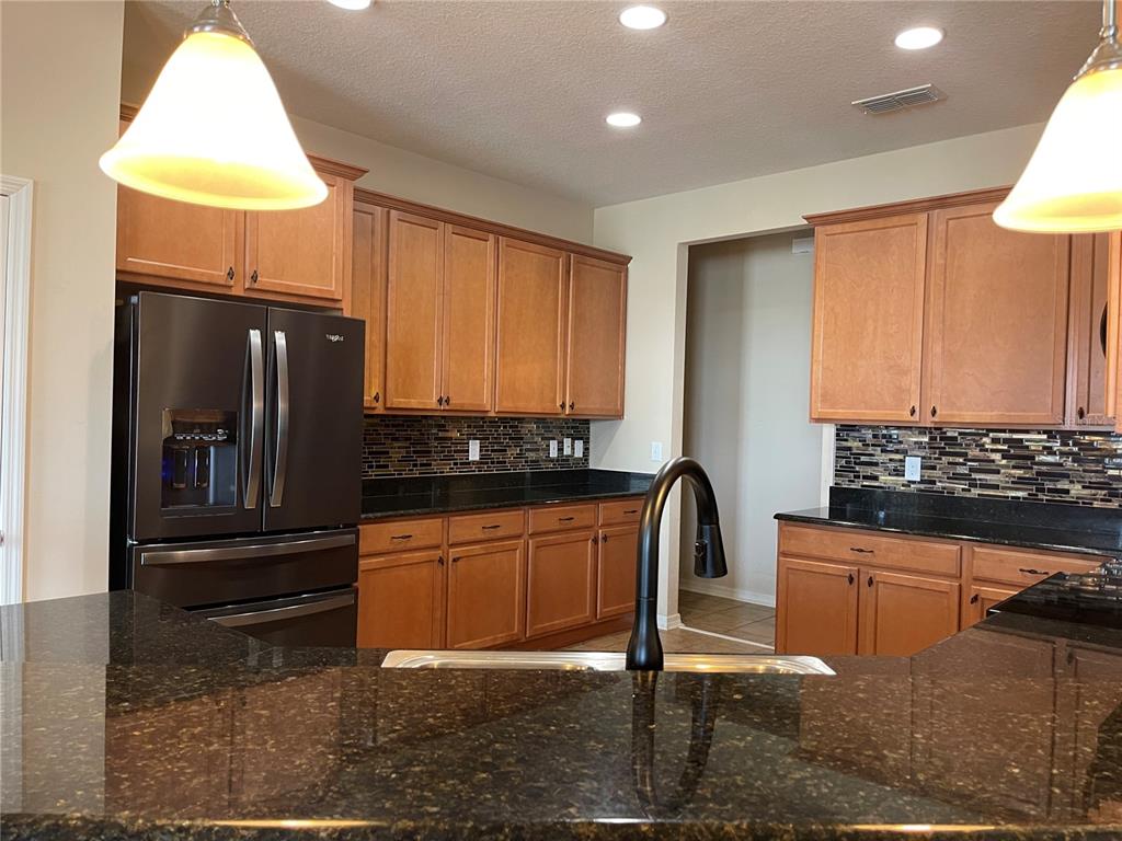 A kitchen features wood cabinets, dark granite countertops, a black refrigerator, and a tiled backsplash — 10026 WEATHERS LOOP, CLERMONT, FL