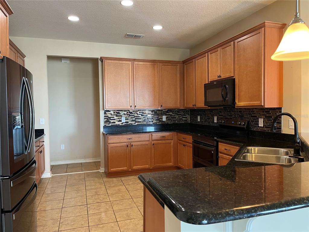 A kitchen features wood cabinets, black granite countertops, a tile backsplash, and stainless steel appliances — 10026 WEATHERS LOOP, CLERMONT, FL