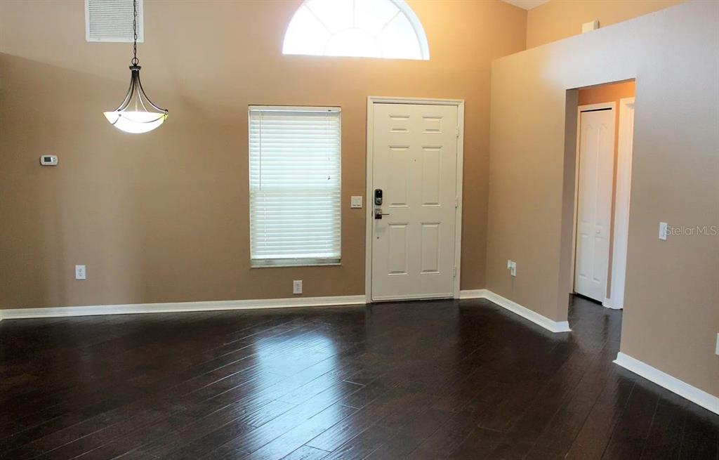A living room with dark wood floors, tan walls, a front door, and a pendant light — 6414 OPEN PASTURE COURT, WESLEY CHAPEL, FL