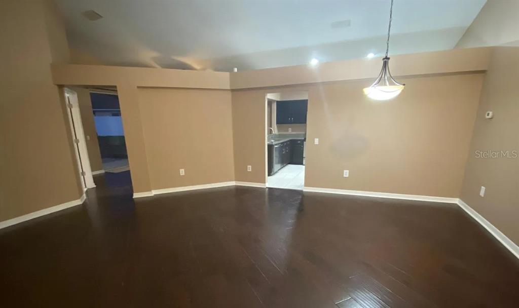 An open living area with dark hardwood floors, beige walls, and a view into the kitchen — 6414 OPEN PASTURE COURT, WESLEY CHAPEL, FL