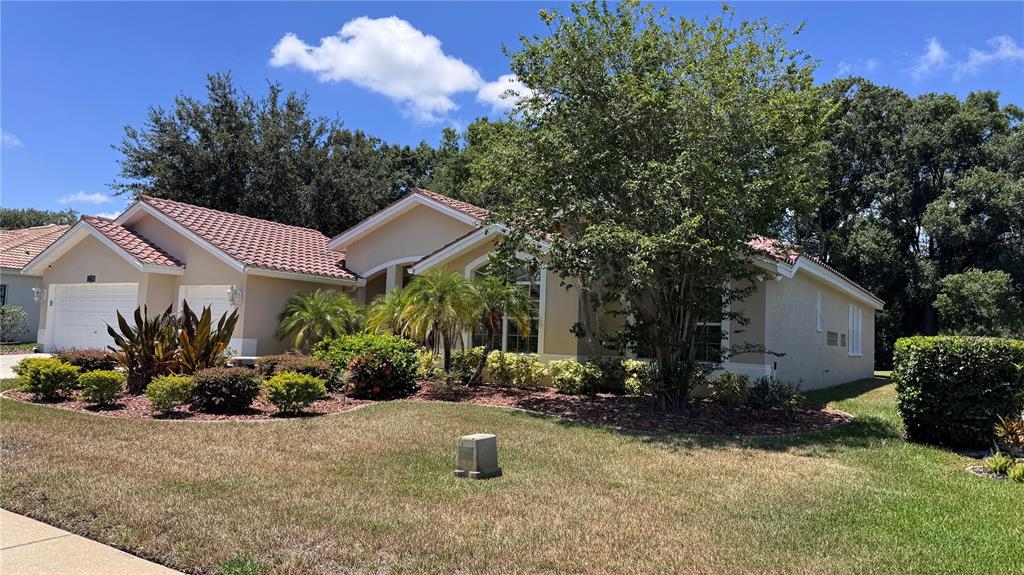 A single-story house with a tiled roof, tan stucco exterior, and landscaped front yard — 1230 BERKSHIRE LANE, TARPON SPRINGS, FL