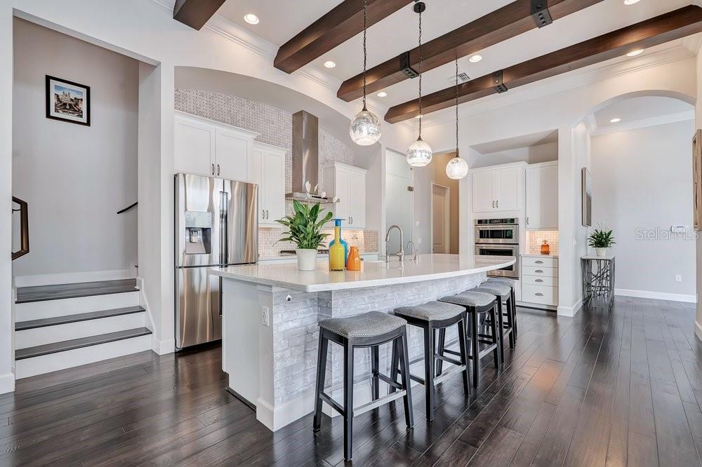 A kitchen with a white island, dark wood floors, exposed ceiling beams, and a glass-enclosed wine cellar — 8449 VIA VITTORIA WAY, ORLANDO, FL