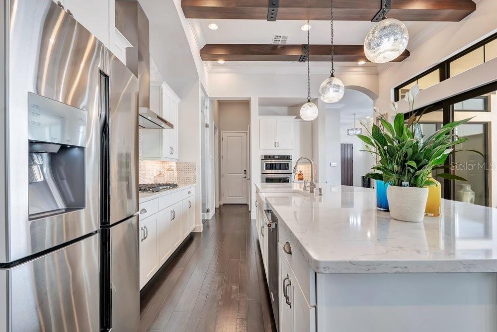 A modern kitchen features white cabinetry, quartz countertops, a farmhouse sink, and dark wood flooring — 8449 VIA VITTORIA WAY, ORLANDO, FL