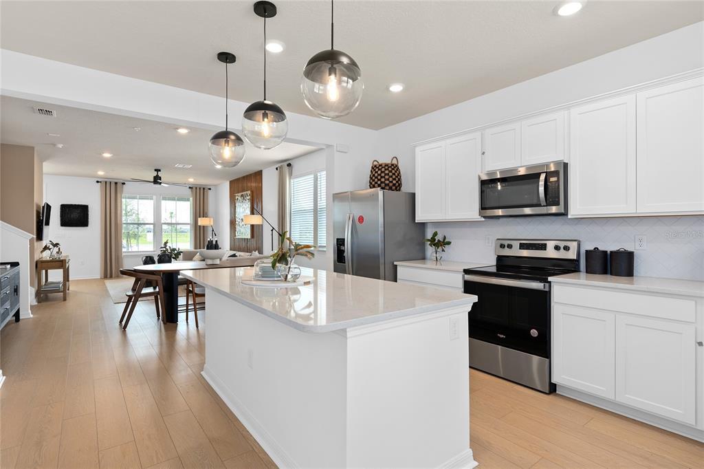A modern kitchen features white cabinets, stainless steel appliances, and a large quartz-topped island — 1151 LEMONGRASS ALLEY, ORLANDO, FL
