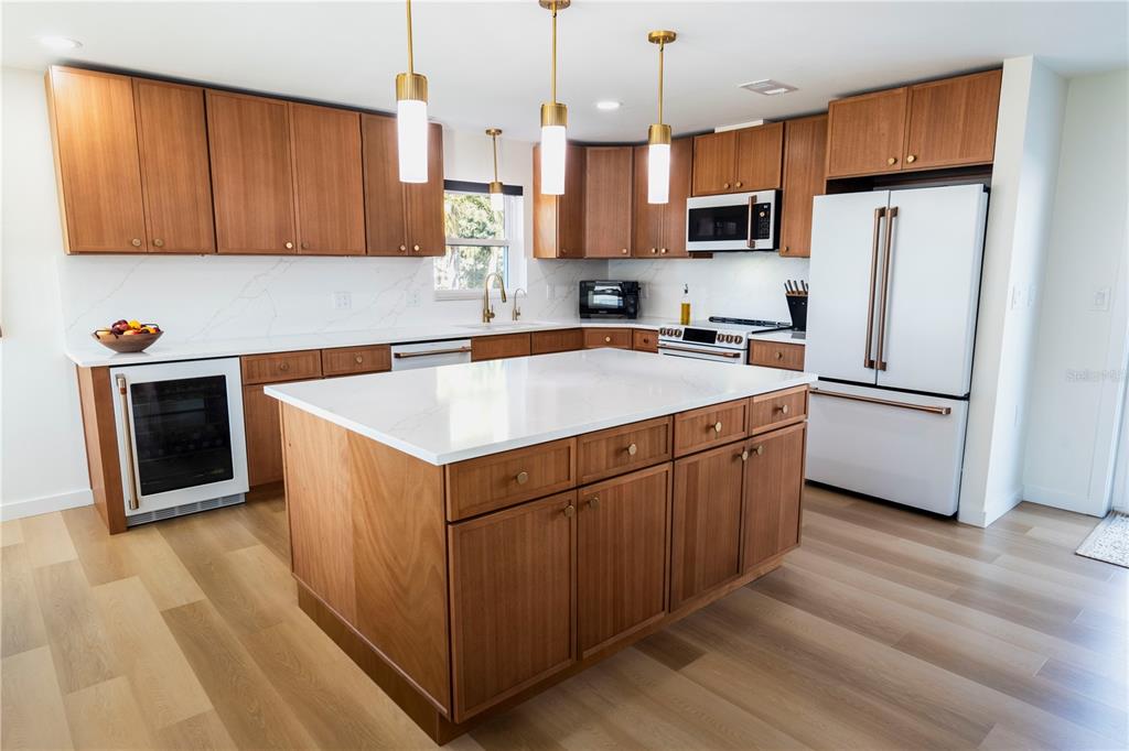 A modern kitchen features wood cabinets, a white quartz island, and stainless steel appliances — 705 GULF BOULEVARD, BELLEAIR BEACH, FL