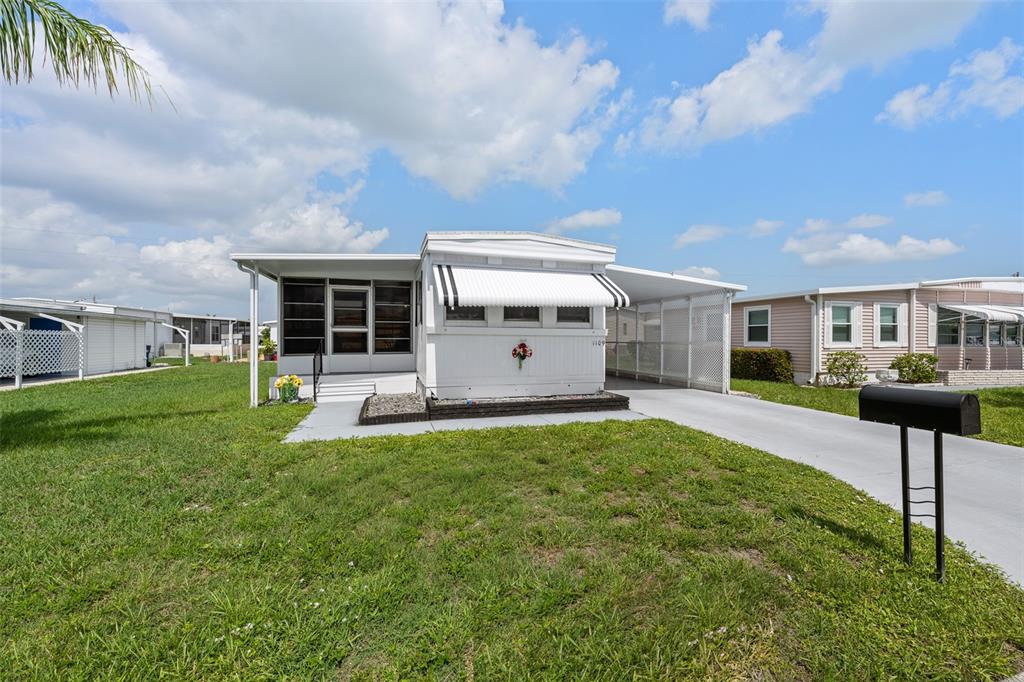 A white manufactured home with a screened porch, carport, and a black mailbox in front — 1109 45TH AVENUE E, ELLENTON, FL