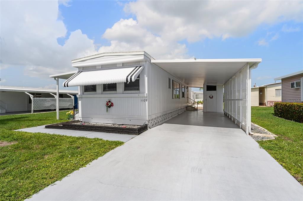 A white mobile home features a concrete driveway, a carport, and a small front garden — 1109 45TH AVENUE E, ELLENTON, FL