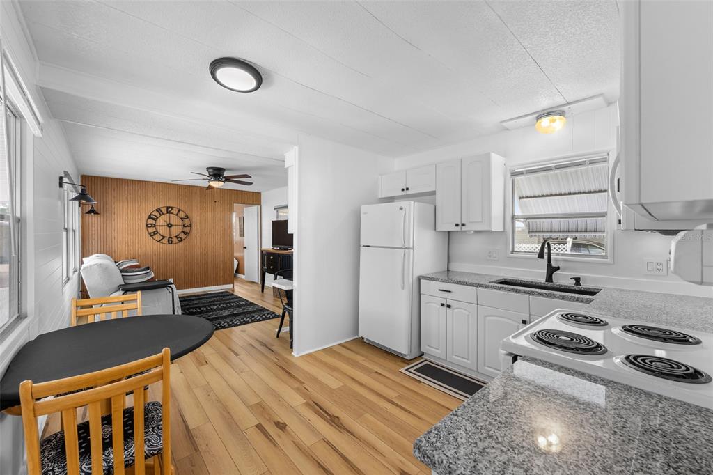 A kitchen with white cabinets and granite countertops opens into a living area with wood-paneled walls — 1109 45TH AVENUE E, ELLENTON, FL