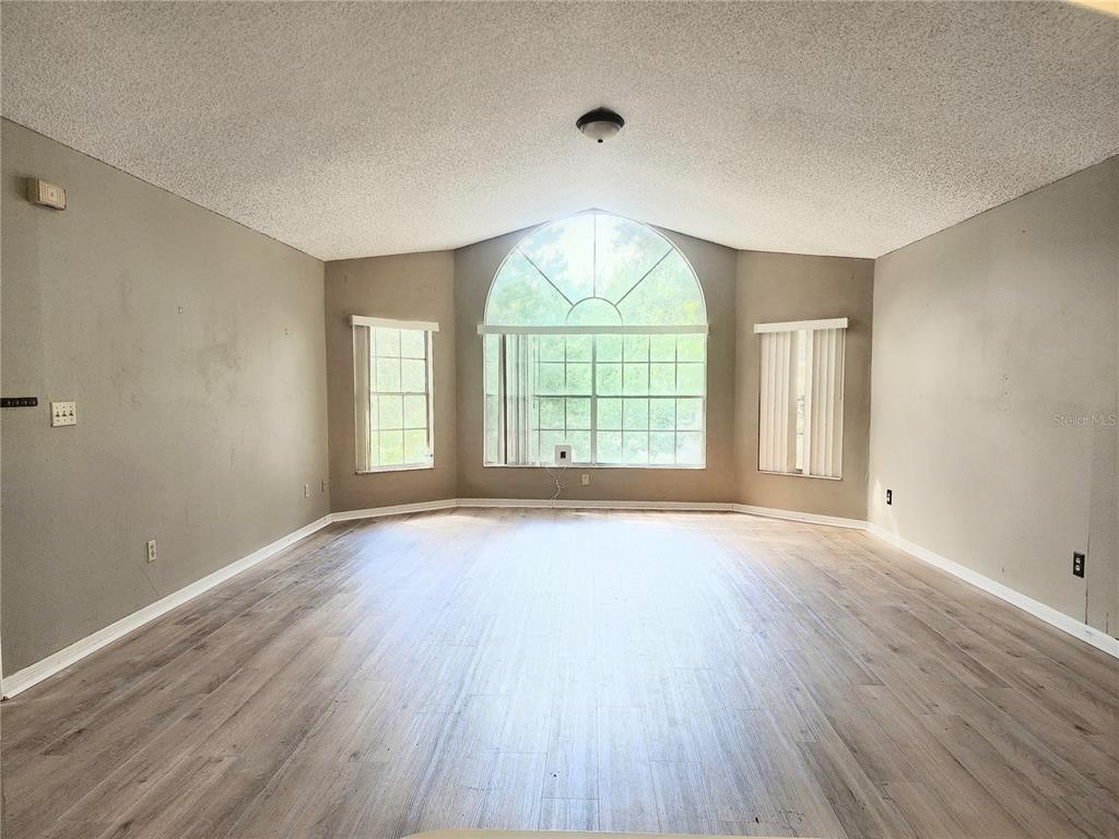 An empty living room with vaulted ceilings, light wood-look flooring, and a large arched window — 2723 N POINCIANA BOULEVARD UNIT 160, KISSIMMEE, FL
