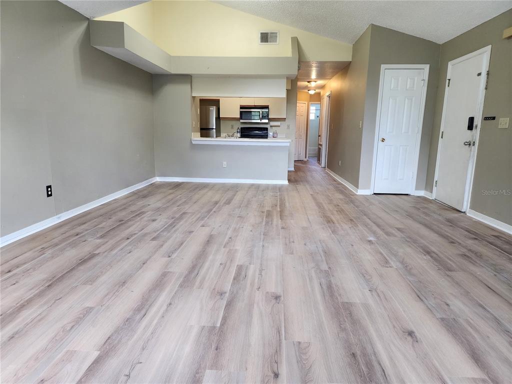 An open-concept living area features light wood-look flooring, vaulted ceilings, and a kitchen pass-through window — 2723 N POINCIANA BOULEVARD UNIT 160, KISSIMMEE, FL