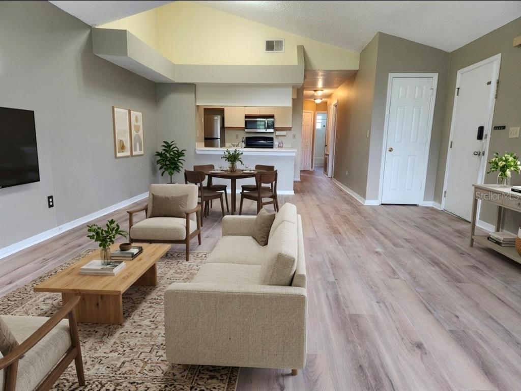 An open-concept living and dining area features light wood flooring, vaulted ceilings, and neutral furniture — 2723 N POINCIANA BOULEVARD UNIT 160, KISSIMMEE, FL
