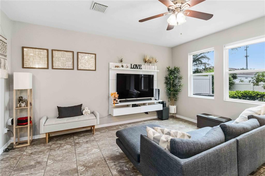A living room features tile flooring, a wall-mounted television console, and a grey sectional sofa — 10716 AVERY PARK DRIVE, RIVERVIEW, FL