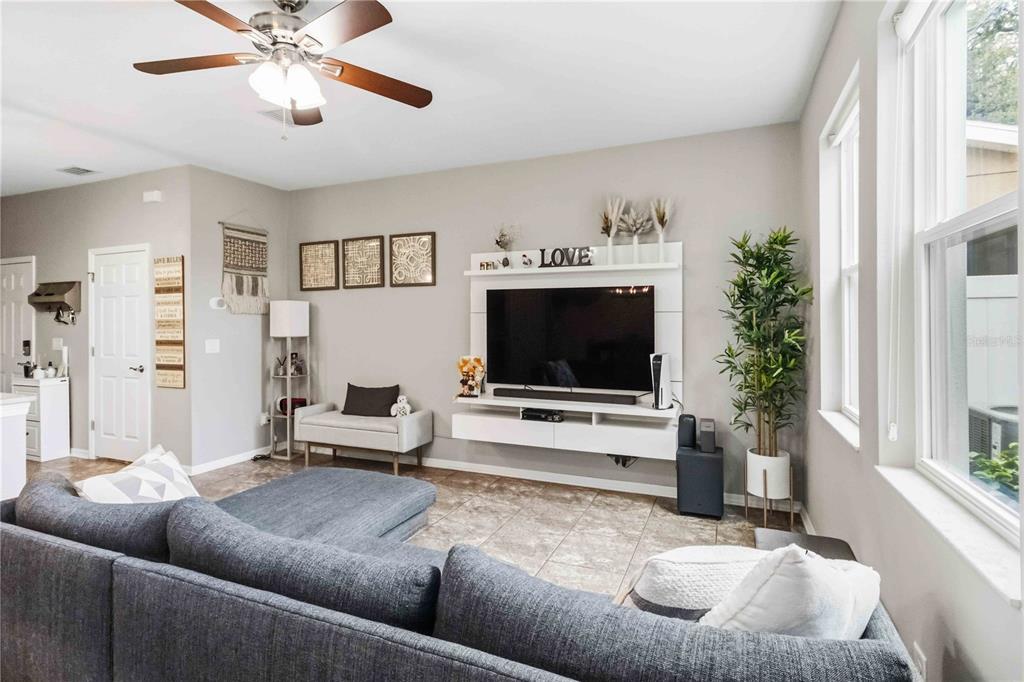 A living room features a grey sectional sofa, a wall-mounted television, and tile flooring — 10716 AVERY PARK DRIVE, RIVERVIEW, FL