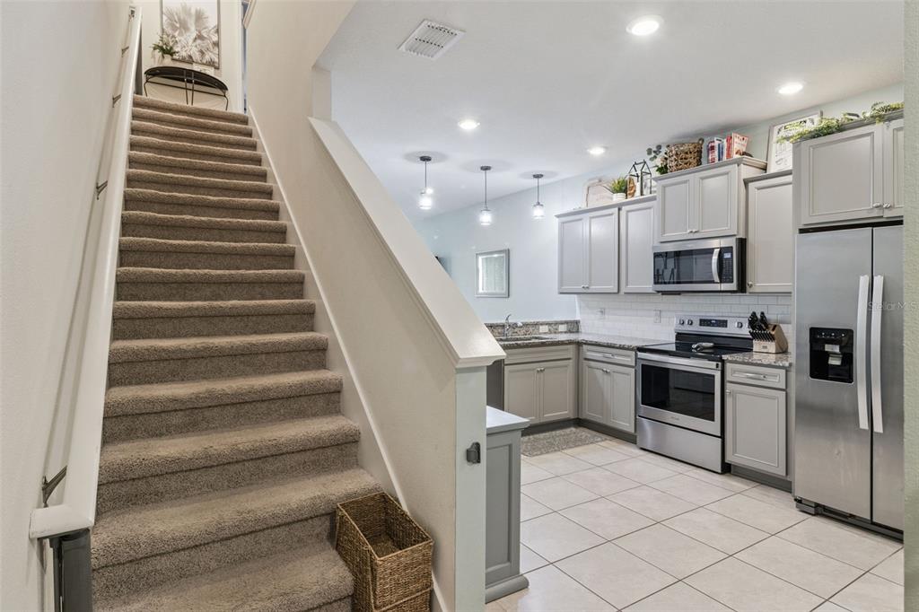 A carpeted staircase leads to an upper level next to a kitchen with gray cabinets — 5329 SYLVESTER LOOP, TAMPA, FL