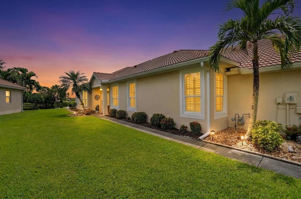A side view of a beige house with a tiled roof, lawn, and palm tree — 5037 WHISPERING OAKS DRIVE, NORTH PORT, FL
