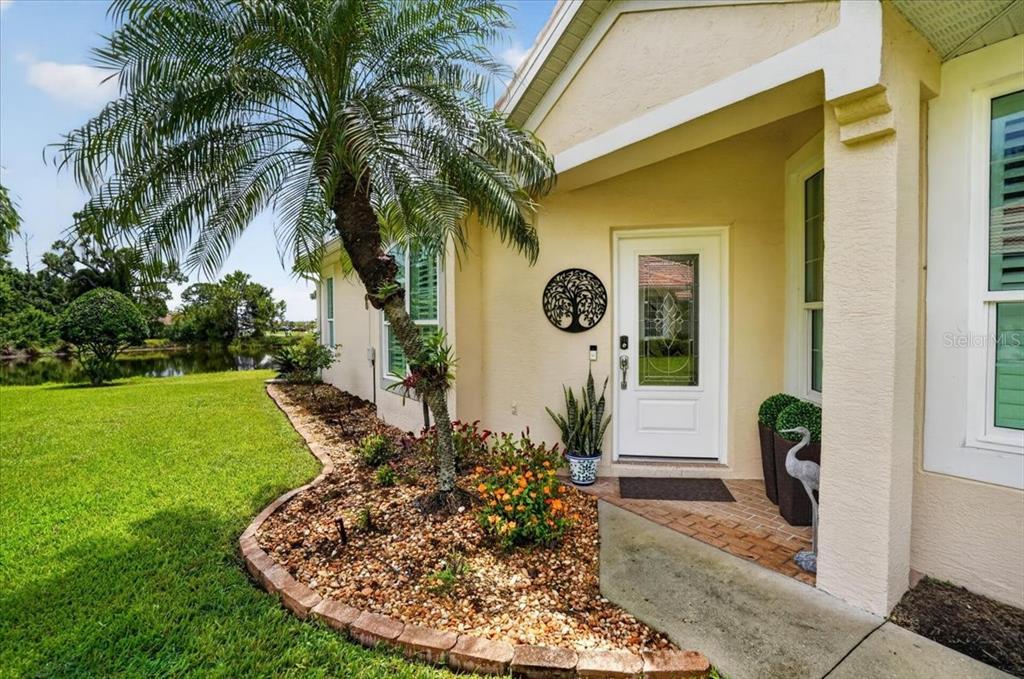A palm tree stands in a landscaped garden bed next to a home's front entrance — 5037 WHISPERING OAKS DRIVE, NORTH PORT, FL