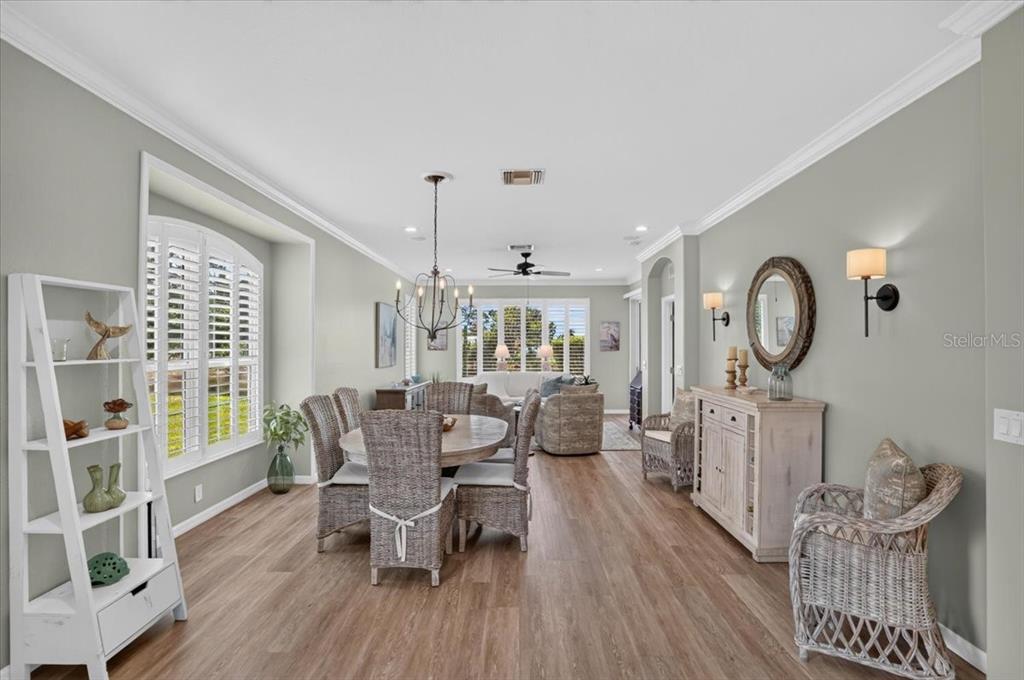 A dining area and living room feature wicker furniture, light wood floors, and plantation shutters — 5037 WHISPERING OAKS DRIVE, NORTH PORT, FL