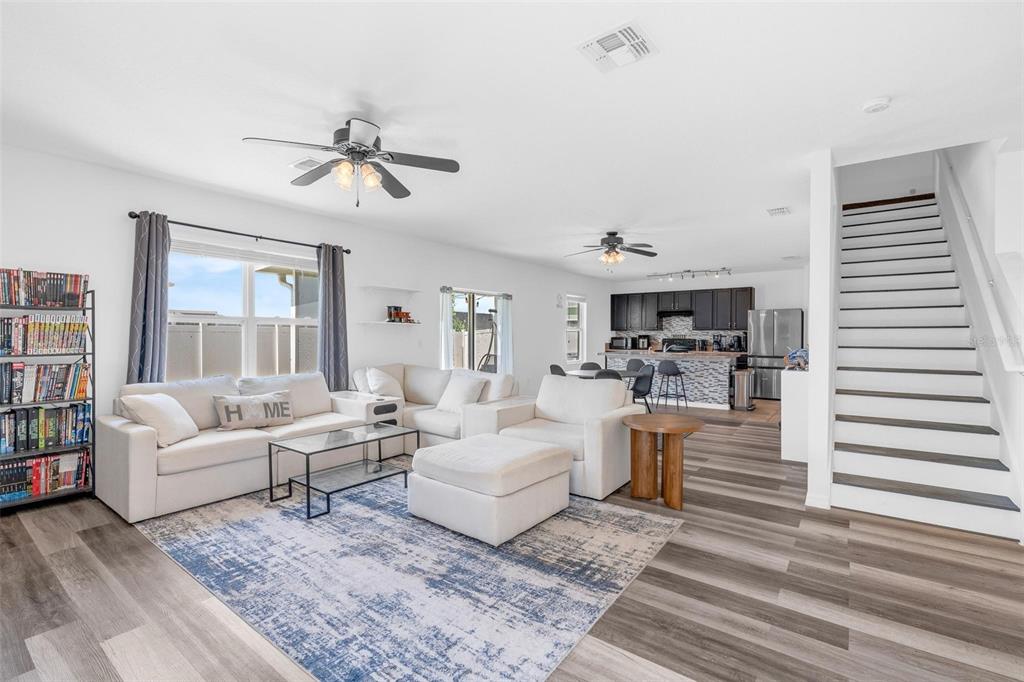 An open-concept living room features white sofas, a patterned rug, and a staircase — 16610 BROADFORD LANE, CLERMONT, FL