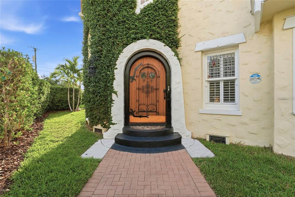 An arched wooden front door with iron detailing is set into a textured yellow stucco wall — 190 BOSPHOROUS AVENUE, TAMPA, FL