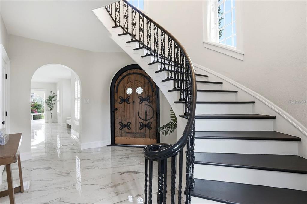 A foyer features a curved staircase with black railings, marble flooring, and an arched wooden door — 190 BOSPHOROUS AVENUE, TAMPA, FL