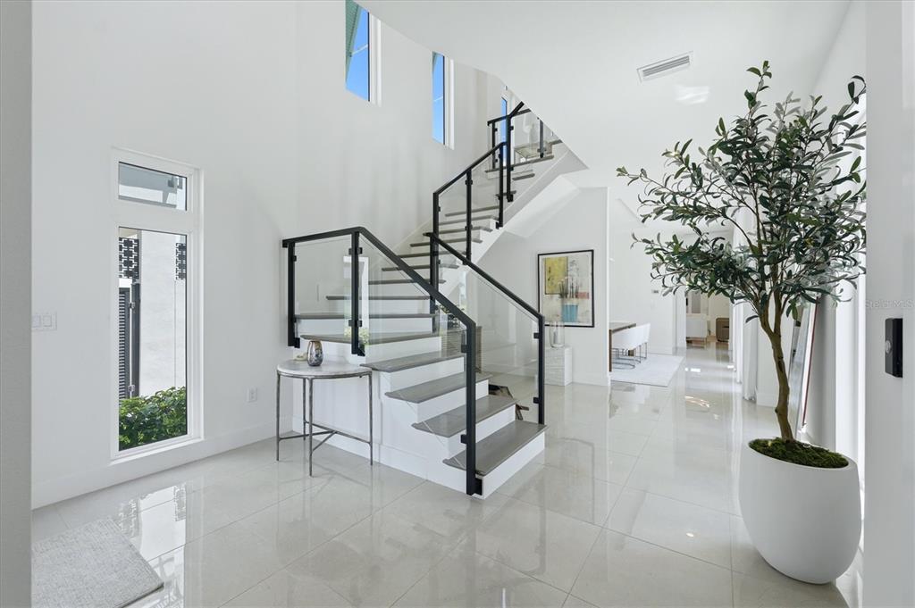 A bright entryway features a modern staircase with glass railings and polished tile flooring — 5935 REDBAY BOULEVARD, BRADENTON, FL