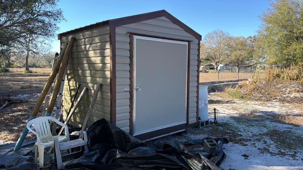 A tan storage shed with a single door sits on a dirt lot outdoors — 0 N KRAFT ROAD, AVON PARK, FL