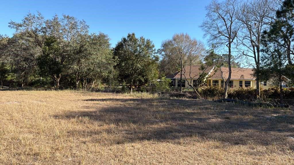 A large, dry, grassy vacant lot sits in front of a house surrounded by trees — 0 N KRAFT ROAD, AVON PARK, FL