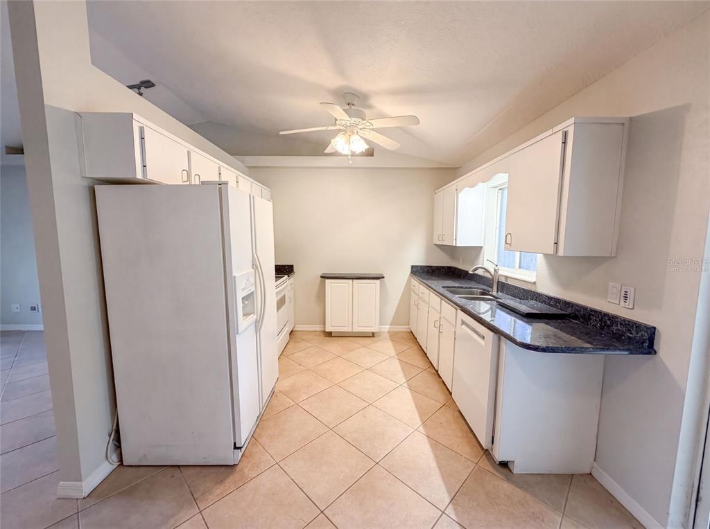 A kitchen features white cabinets, dark countertops, a white refrigerator, and light-colored tile flooring — 1719 NEEDLE PALM DRIVE, EDGEWATER, FL