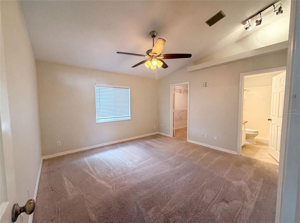 A bedroom with beige carpet, a ceiling fan, a window, a closet, and an attached bathroom — 1719 NEEDLE PALM DRIVE, EDGEWATER, FL
