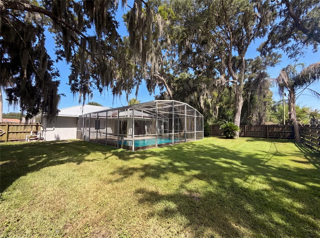 A backyard features a screened-in swimming pool, a grassy lawn, and large moss-draped trees — 1719 NEEDLE PALM DRIVE, EDGEWATER, FL