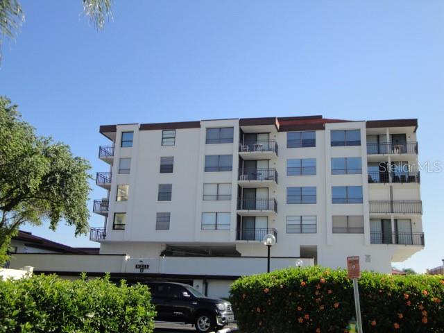 A multi-story apartment building with balconies stands behind a dark vehicle and green bushes — 6211 SUN BOULEVARD UNIT 215, ST PETERSBURG, FL