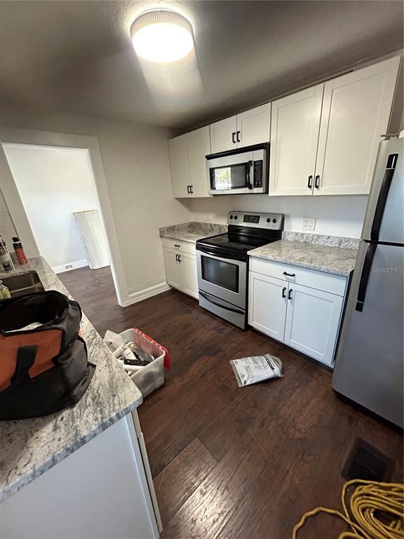 A kitchen features white cabinets, stainless steel appliances, granite countertops, and dark wood-look flooring — 2321 TRELAIN DRIVE S, ST PETERSBURG, FL