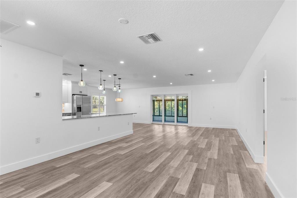 A bright, open-concept living area with wood-look flooring, a kitchen island, and sliding glass doors — 4390 6TH ISLE DRIVE, HERNANDO BEACH, FL