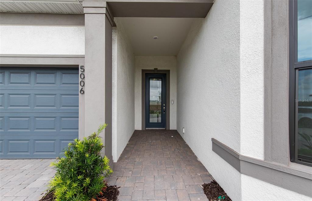 A paved walkway leads to the front entrance of a house with a blue door — 5006 GOLDEN SHORE COURT, LAKEWOOD RANCH, FL