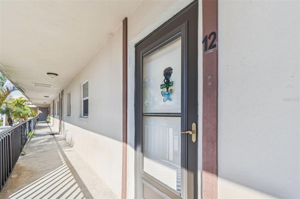An exterior view of an apartment building walkway with a door marked number 12 — 2750 E BAY DRIVE UNIT 12B, LARGO, FL