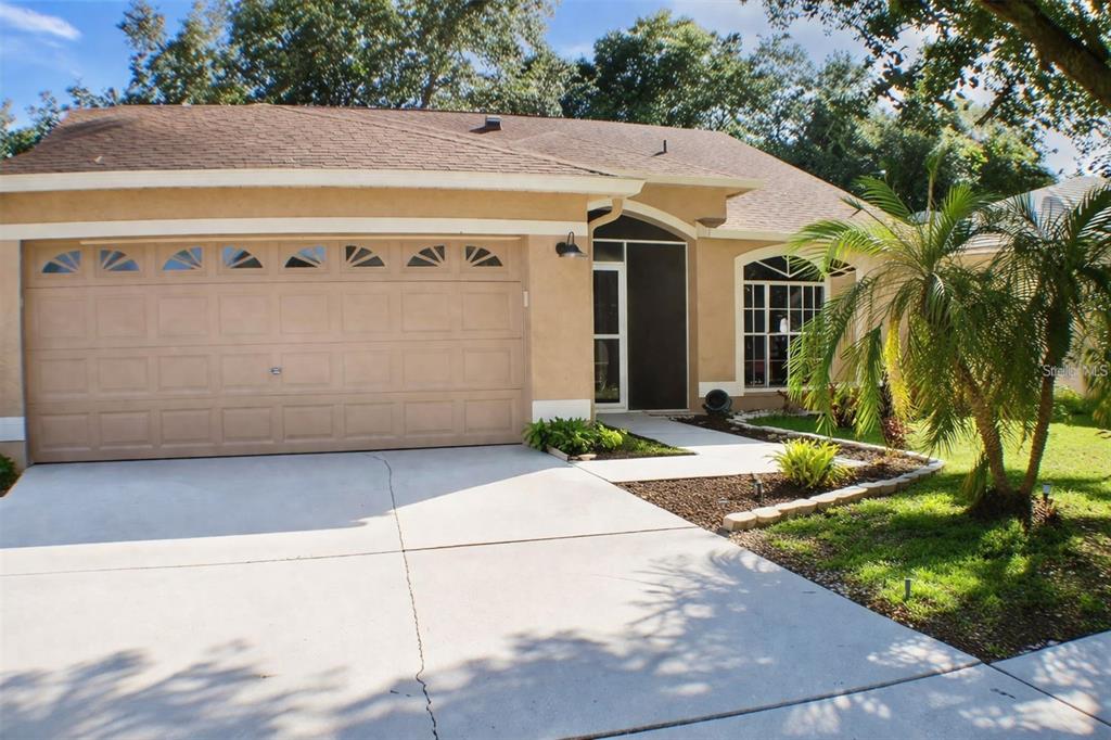 A tan single-story house with a two-car garage, arched window, and a palm tree — 1723 BELL RANCH STREET, BRANDON, FL