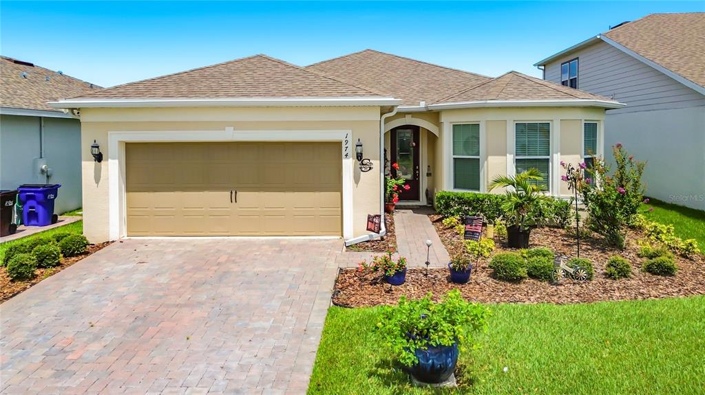A single-story house with a tan exterior, a two-car garage, and a landscaped front yard — 1974 SPRING SHOWER CIRCLE, KISSIMMEE, FL