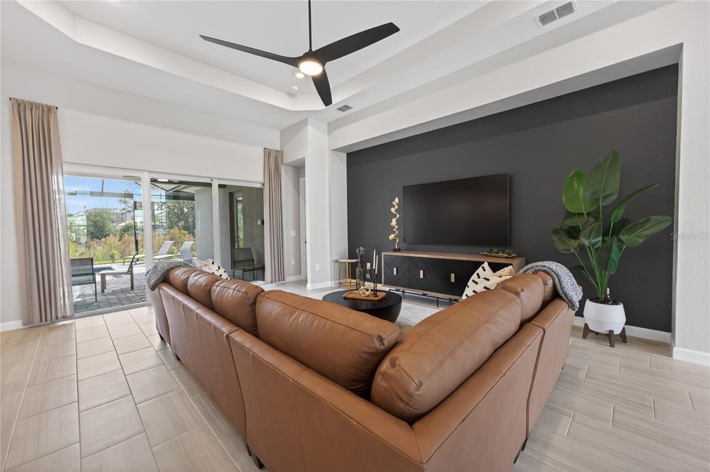 A living room features a brown leather sectional, a dark accent wall, and sliding glass doors — 18731 CHERRYSTONE WAY, BRADENTON, FL