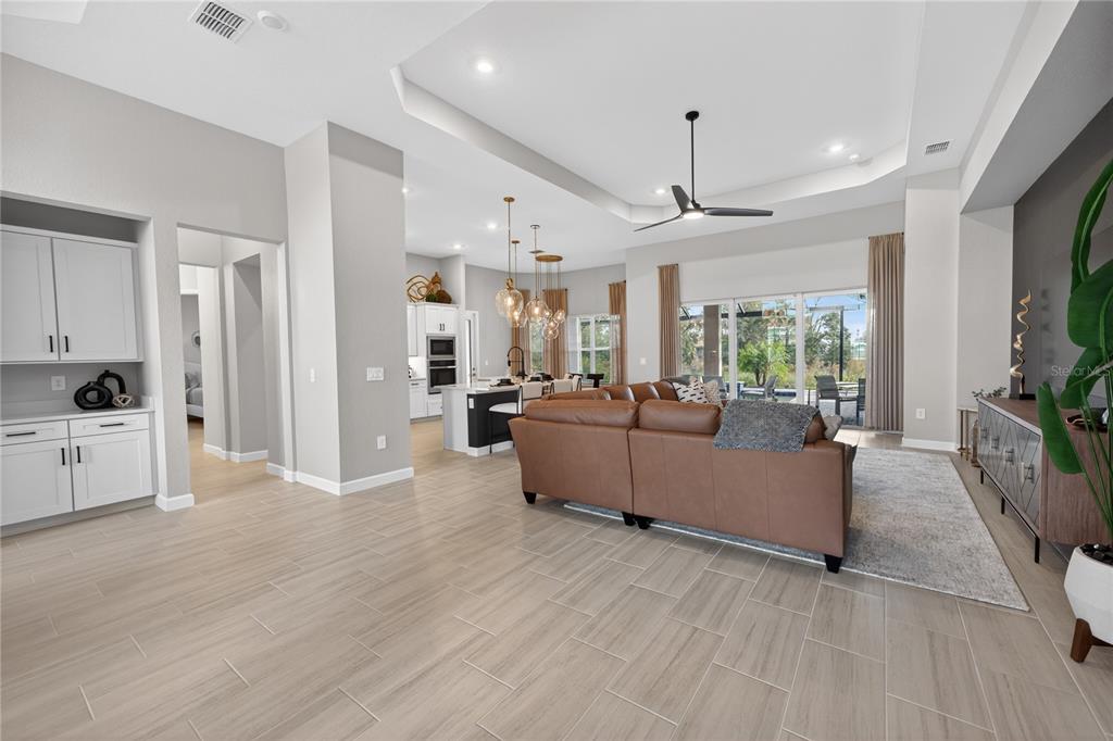 An open-concept living room and kitchen featuring light tile floors and a brown sectional sofa — 18731 CHERRYSTONE WAY, BRADENTON, FL