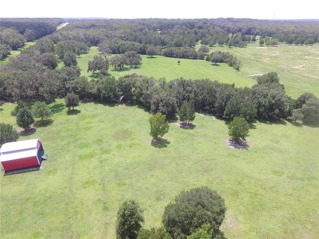 An aerial view shows a red barn on a large, grassy pasture with scattered trees — 11077 PONCE DE LEON BOULEVARD, BROOKSVILLE, FL