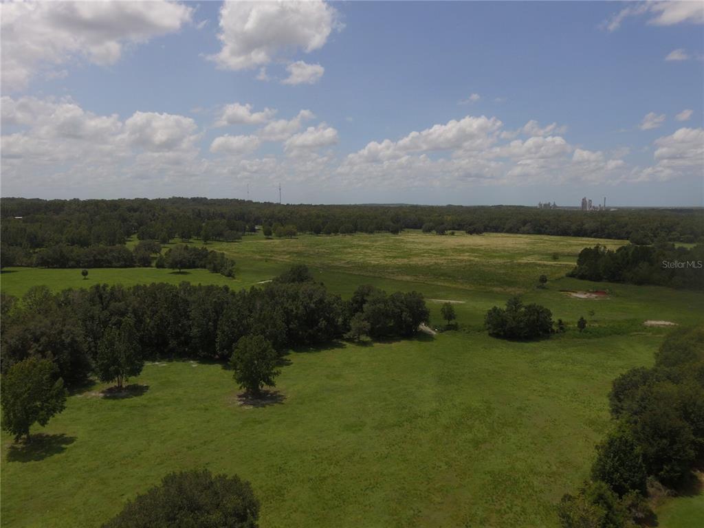 An aerial view shows a large, grassy field surrounded by trees under a cloudy sky — 11077 PONCE DE LEON BOULEVARD, BROOKSVILLE, FL