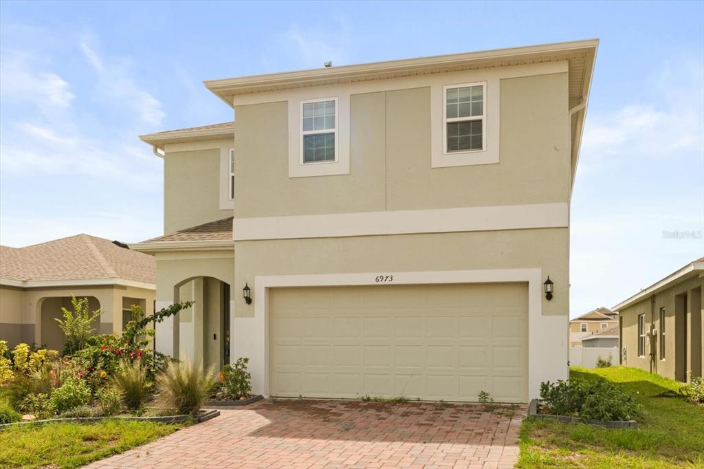 A two-story house with a beige stucco exterior, a two-car garage, and a brick driveway — 6973 WILSON PASTURE AVENUE, GROVELAND, FL