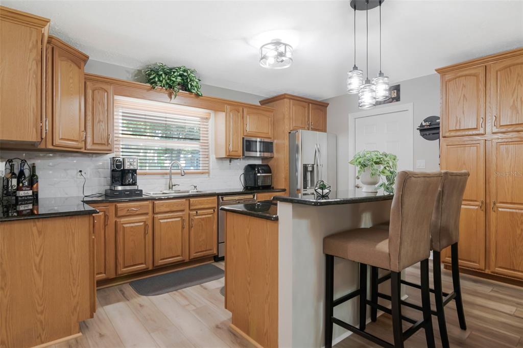 A kitchen features oak cabinets, black granite countertops, stainless steel appliances, and a breakfast bar — 1912 MAY STREET, BRANDON, FL