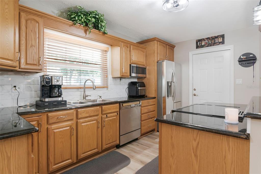 A kitchen with oak cabinets, black granite countertops, stainless steel appliances, and wood-look flooring — 1912 MAY STREET, BRANDON, FL