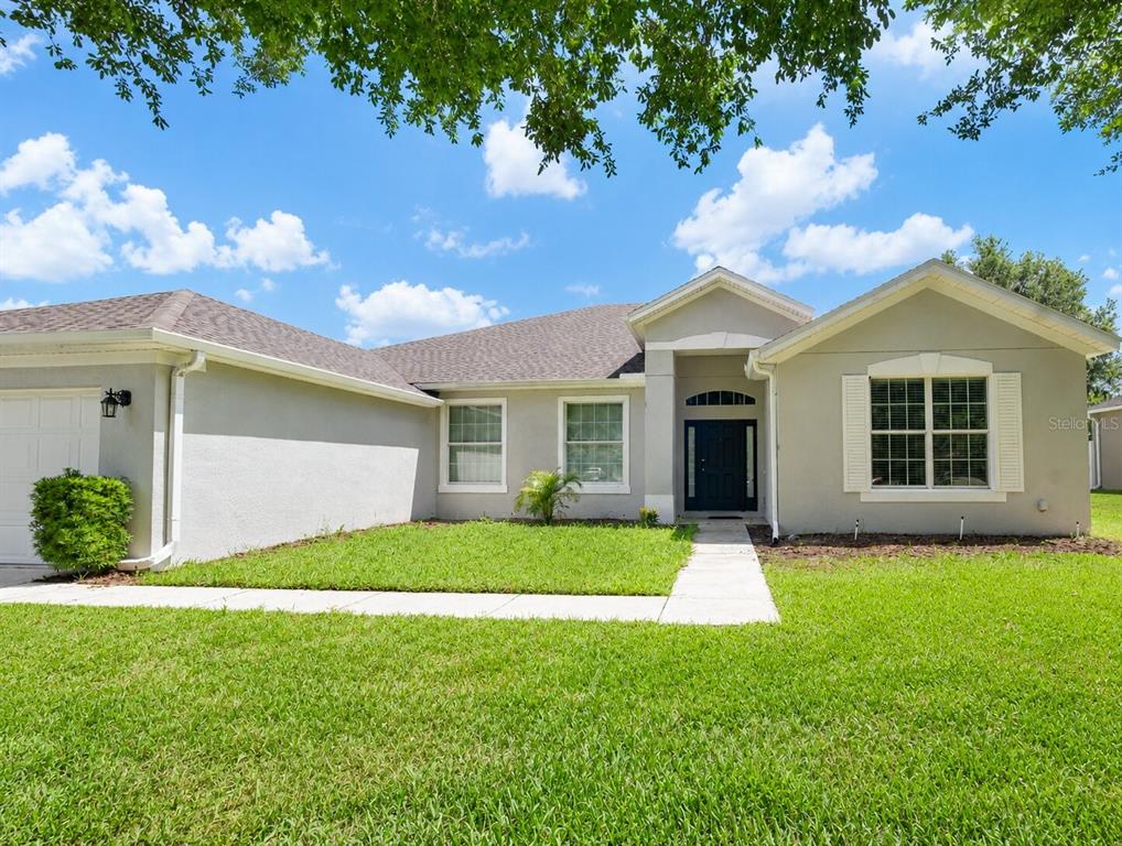 A single-story house with a beige stucco exterior, a dark front door, and a lawn — 1147 DEGRAW DRIVE, APOPKA, FL