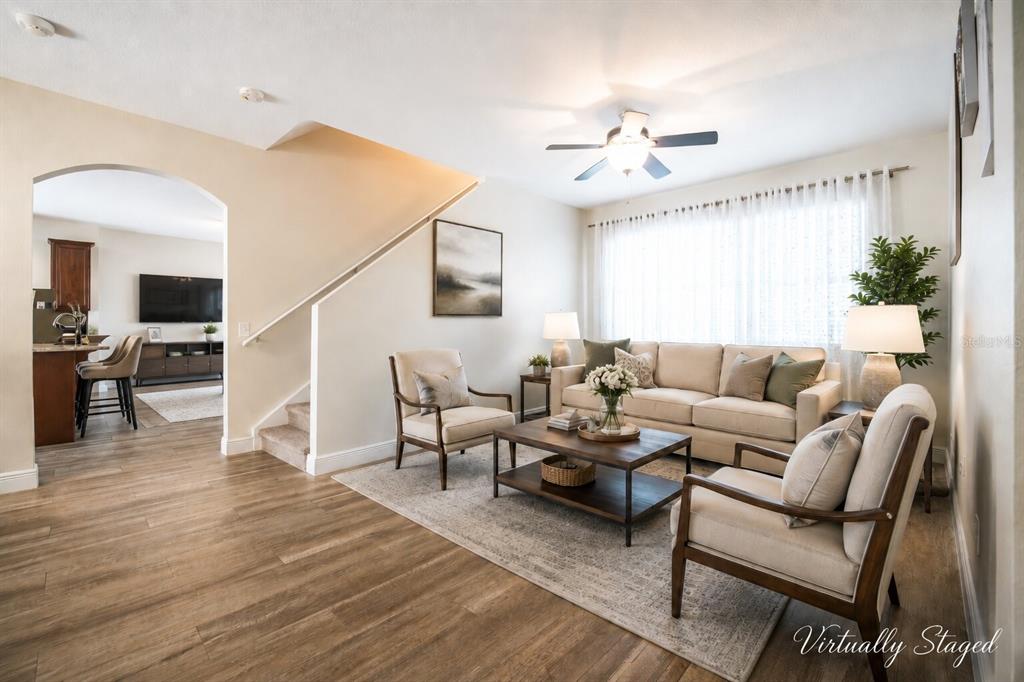 A living room with wood-look flooring, a staircase, and neutral furniture is virtually staged — 1147 DEGRAW DRIVE, APOPKA, FL