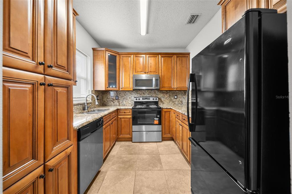 A kitchen features wooden cabinets, granite countertops, stainless steel appliances, and tile flooring — 18171 PARADISE POINT DRIVE, TAMPA, FL