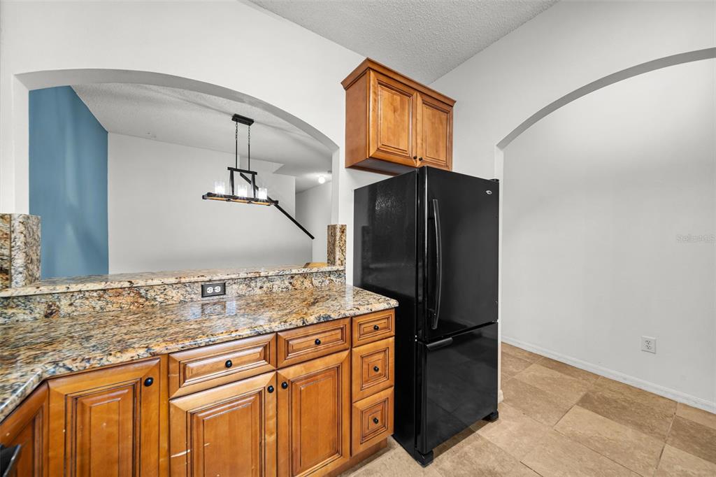 A kitchen with wood cabinets, granite countertops, and a black refrigerator under an arched opening — 18171 PARADISE POINT DRIVE, TAMPA, FL